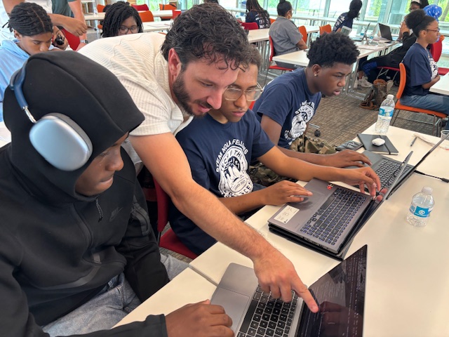 a teacher points at a laptop screen of a student in a classroom